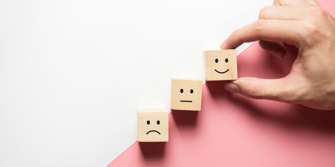 Sad, indifferent, and happy faces on wooden squares, indicating patient satisfaction.